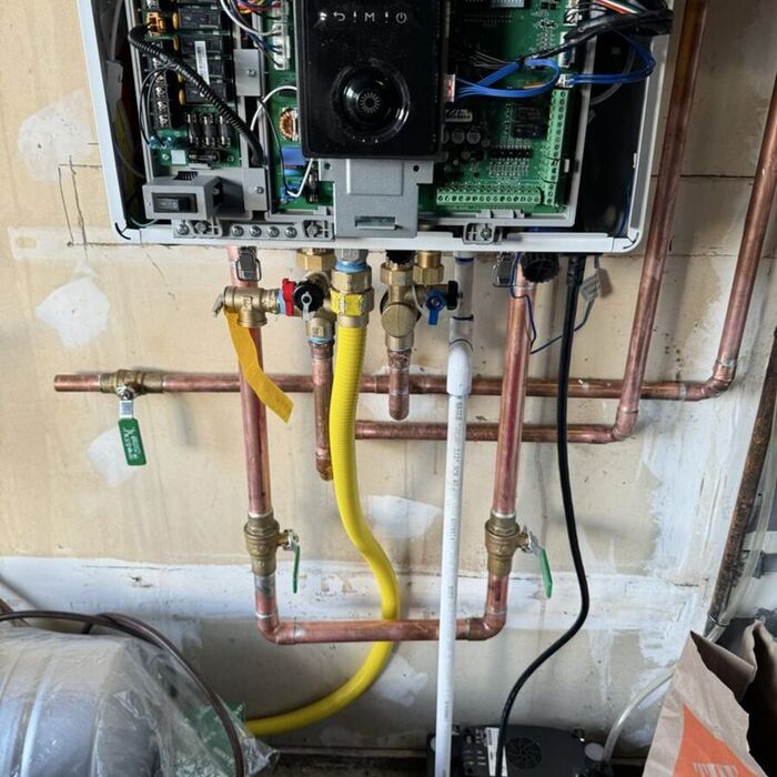Licensed technician wiring a Rinnai tankless water heater control board with copper and PEX supply lines