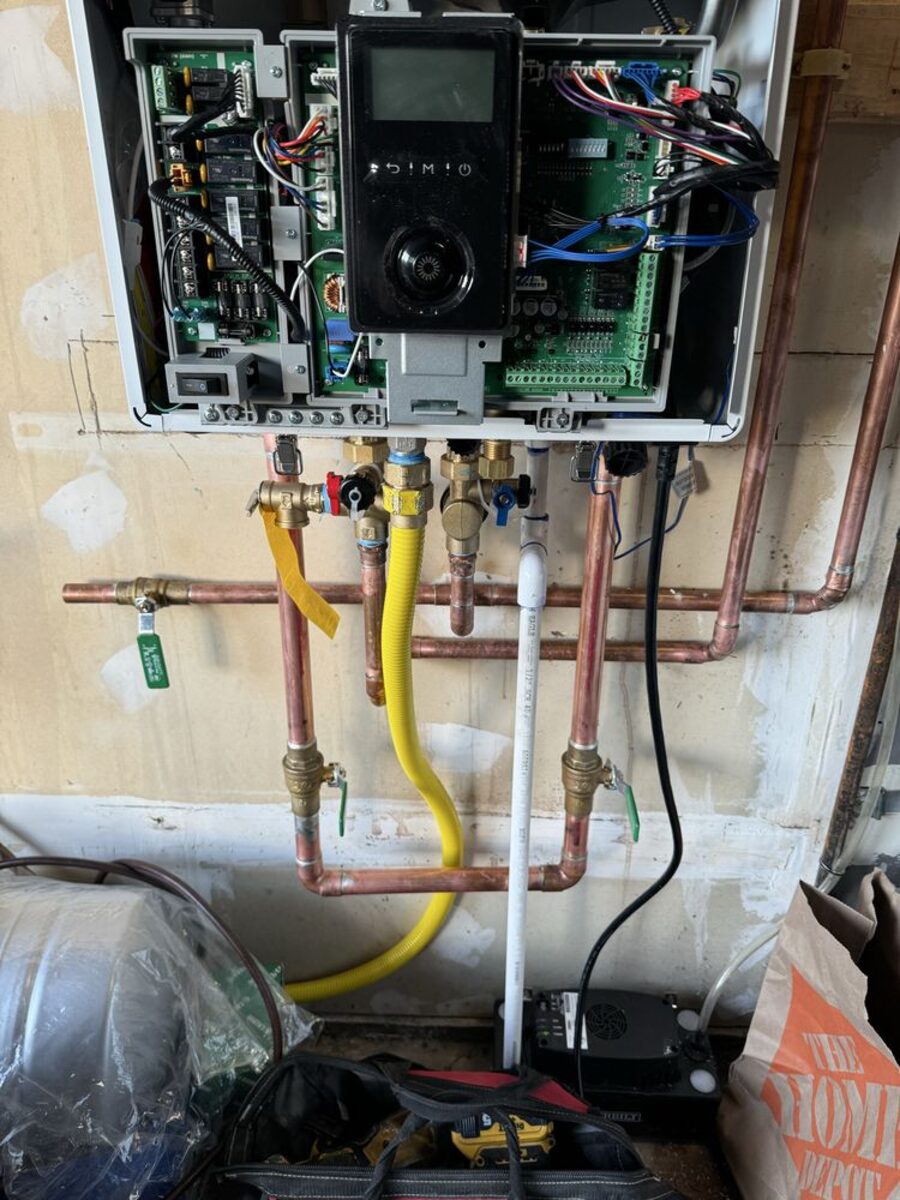 Licensed technician wiring a Rinnai tankless water heater control board with copper and PEX supply lines